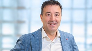 News Porträt eines lächelnden Mannes mit blauem Sakko vor hellem Hintergrund