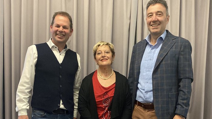 Riunione circondariale di Bolzano: focus sulla promozione dei giovani talenti e sui progetti infrastrutturali Tre persone sorridenti davanti a una tenda, due uomini e una donna