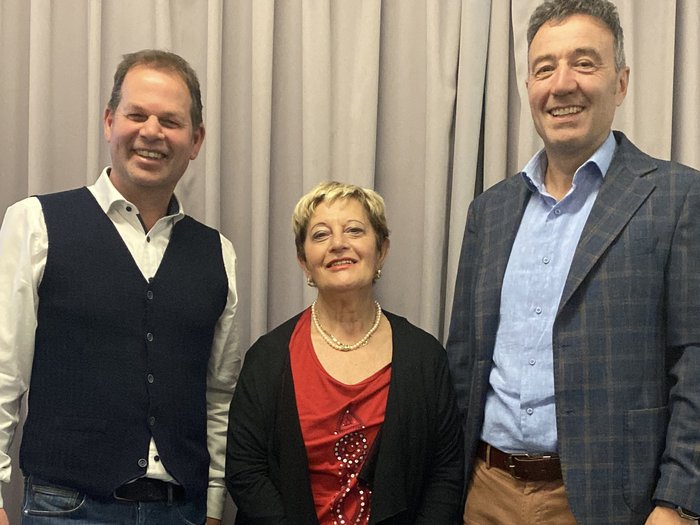 Riunione circondariale di Bolzano: focus sulla promozione dei giovani talenti e sui progetti infrastrutturali Tre persone sorridenti davanti a una tenda, due uomini e una donna