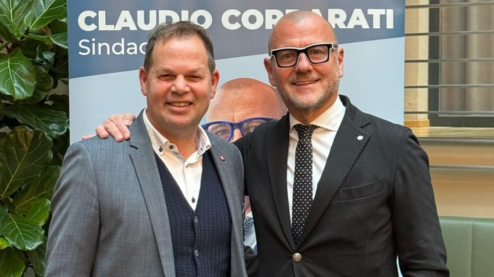 „Gemeindewahlen in Bozen: eine starke Stimme für das Handwerk“ Zwei Männer in Anzügen vor einem Wahlplakat von Claudio Corrarati