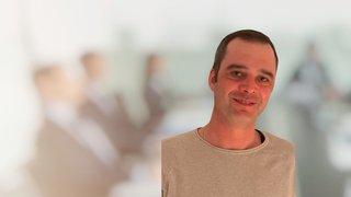 News Lächelnder Mann im Vordergrund mit unscharfer Gruppe hinter ihm