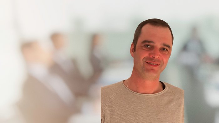 Neuer Ortsobmann für das Handwerk in Kaltern Lächelnder Mann im Vordergrund mit unscharfer Gruppe hinter ihm