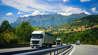 News Lastwagen fahren auf Autobahn vor Bergkulisse und grünem Wald