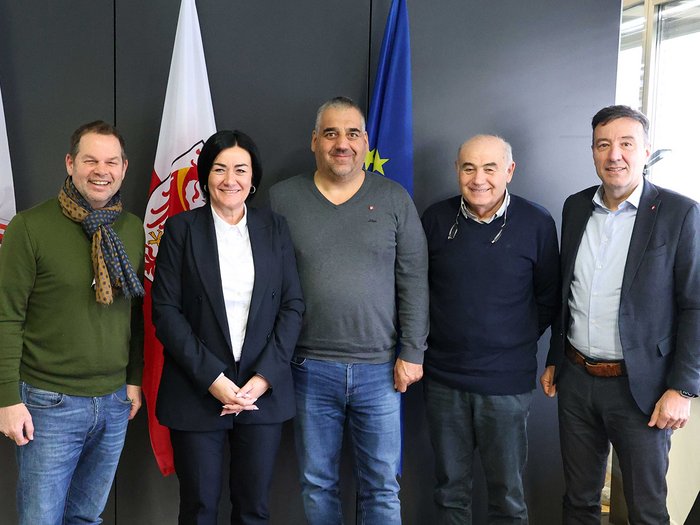 Il settore dell‘autonoleggio a confronto con l’Assessora provinciale Ulli Mair Cinque persone in piedi davanti a bandiere sorridono in un ufficio