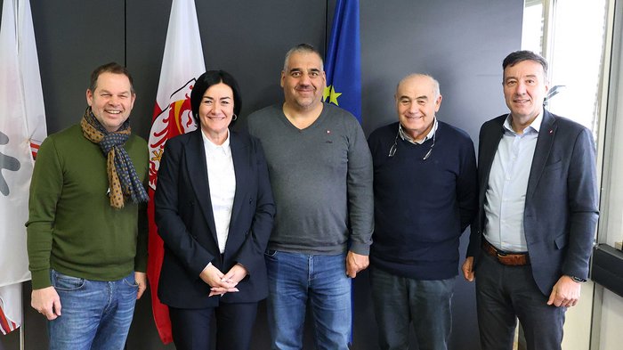 Un sostegno di valore durante la pandemia Cinque persone in piedi davanti a bandiere sorridono in un ufficio