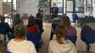 News Jugendliche im Klassenzimmer hören Vortrag von zwei Personen mit Mundschutz