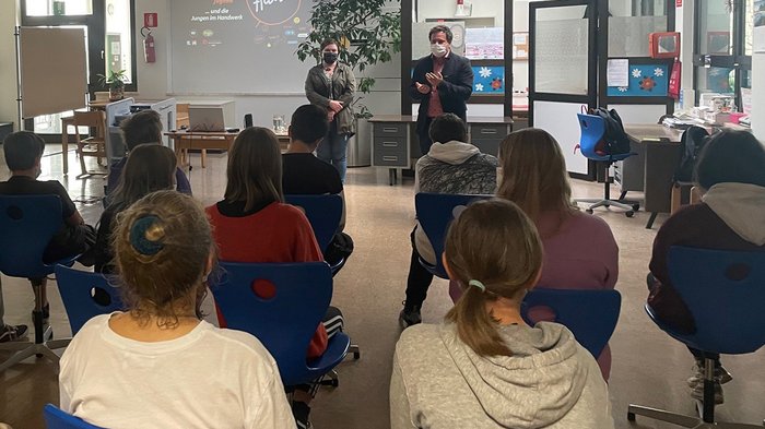 In die Welt der praktischen Berufe eintauchen Jugendliche im Klassenzimmer hören Vortrag von zwei Personen mit Mundschutz