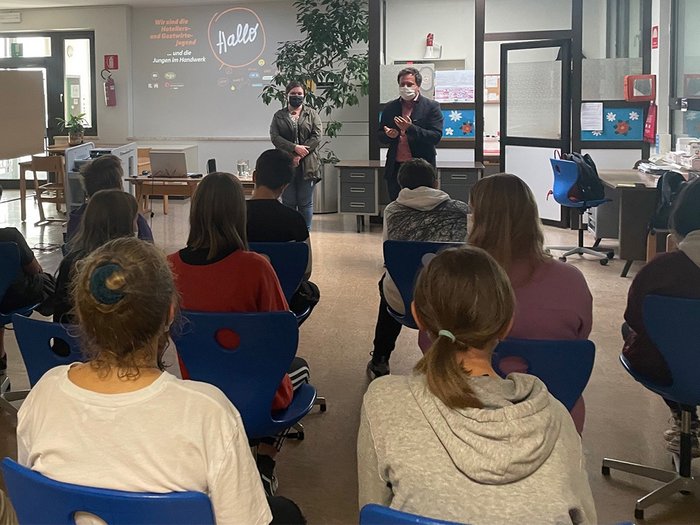 In die Welt der praktischen Berufe eintauchen Jugendliche im Klassenzimmer hören Vortrag von zwei Personen mit Mundschutz