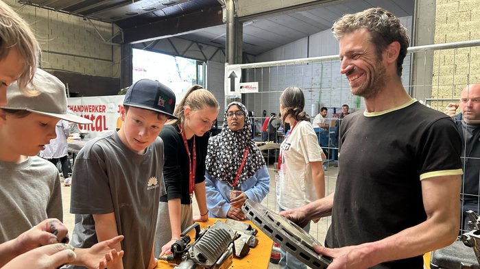 SkillsDay nella Val d'Ega: scoprire l'artigianato, scoprire talenti Uomo spiega ai bambini apparecchi tecnologici su tavolo in magazzino