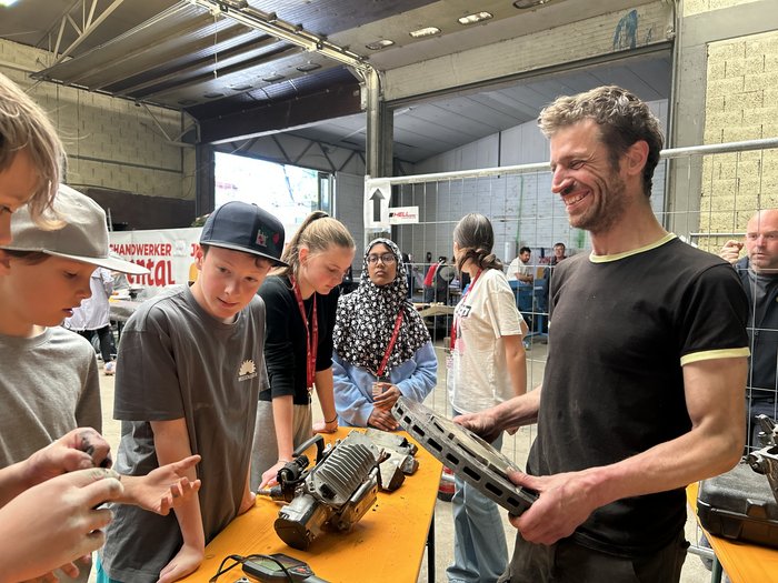 SkillsDay nella Val d'Ega: scoprire l'artigianato, scoprire talenti Uomo spiega ai bambini apparecchi tecnologici su tavolo in magazzino