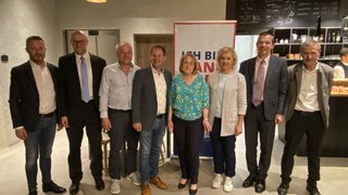 News Gruppe von acht Personen in formeller Kleidung in einem Innenraum vor einem Werbebanner