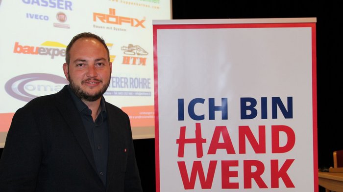 Südtiroler Tiefbauunternehmer/innen: Michael Hofer als Obmann bestätigt Mann steht neben Schild mit Schrift Ich bin Handwerk