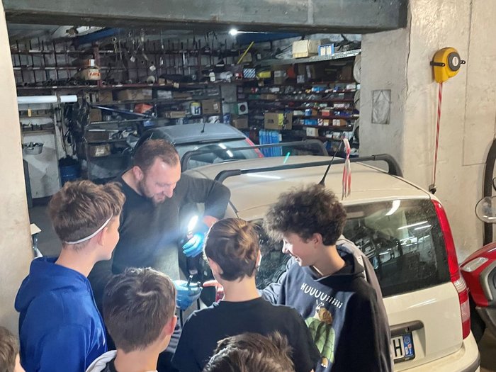 Einblicke in den Berufsalltag Mann zeigt Gruppe junger Männer Autoteile in einer Garage