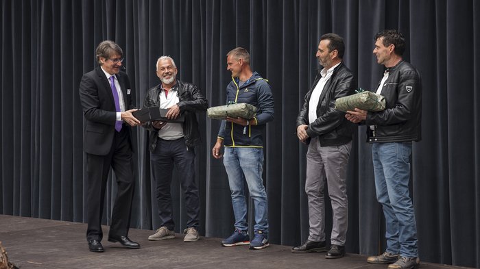Cassa Edile della Provincia Autonoma di Bolzano: premiazione iscritti “30 anni di fiducia“ Uomini sulla scena che ricevono regali durante un evento davanti a una tenda
