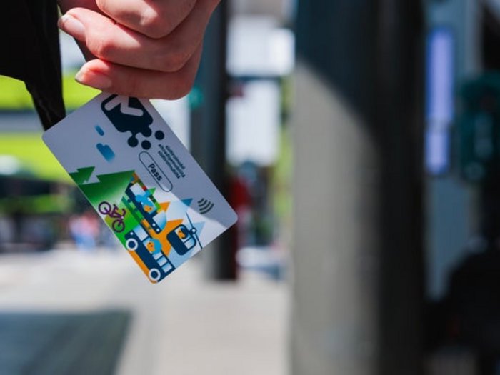Neues Online-Portal für Aktivierung und Verlängerung des südtirolmobil U19 Pass Hand hält Nahverkehrsticket mit buntem Stadtverkehrsdesign