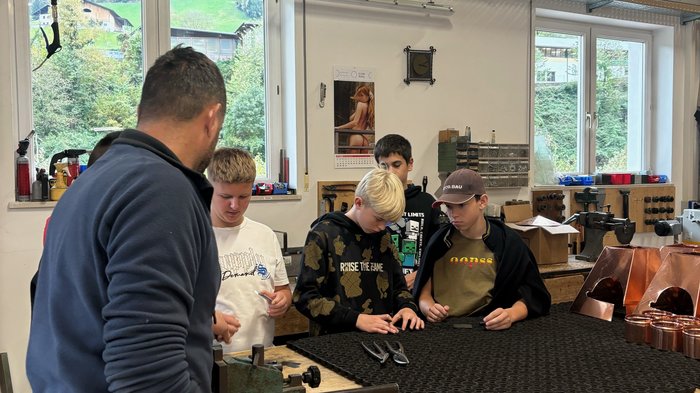 Berufsinformationskampagne St. Martin in Passeier Erwachsener zeigt Jugendlichen Werkzeuge und Arbeitstisch in Werkstatt