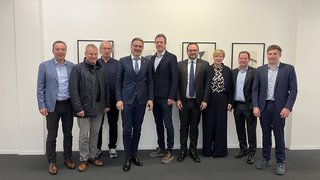 News Neun Personen in Anzügen stehend vor einer weißen Wand mit Bildern