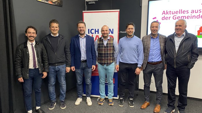 Solides Handwerk in Bruneck Sieben Männer stehen nebeneinander vor Werbebannern und lächeln in die Kamera