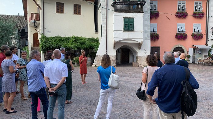 © Plattform Land Gruppe von Menschen hört einer Frau in rotem Kleid auf einem Platz vor historischen Gebäuden zu