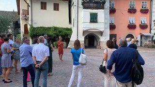 © Plattform Land Gruppe von Menschen hört einer Frau in rotem Kleid auf einem Platz vor historischen Gebäuden zu