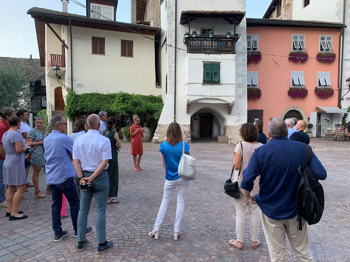 © Plattform Land Gruppe von Menschen hört einer Frau in rotem Kleid auf einem Platz vor historischen Gebäuden zu