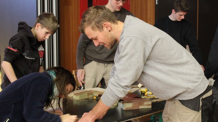 Tag des Handwerks in Jenesien Gruppe junger Menschen arbeitet gemeinsam an Holzprojekten in Innenraum
