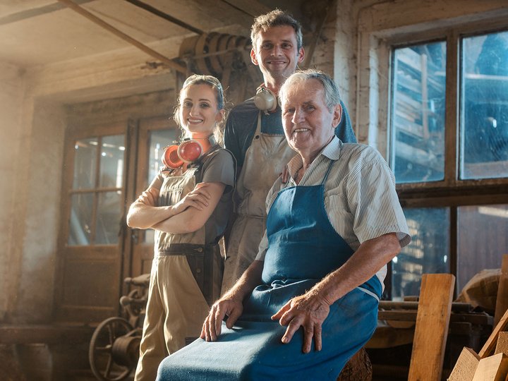 Lavorare deve convenire! Tre falegnami sorridenti in officina con abbigliamento da lavoro