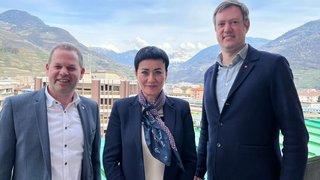 News Drei Personen in Businesskleidung mit Berglandschaft im Hintergrund