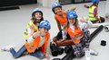 Vivere una giornata in cantiere Bambini con caschi e giubbotti di sicurezza posano con tubi facendo il segno del pollice in su