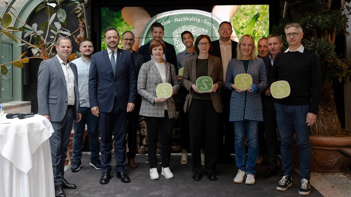 Nachhaltigkeitslabel Südtirol Gruppenfoto von zwölf Personen bei einer Auszeichnung mit nachhaltigen Zertifikatstafeln