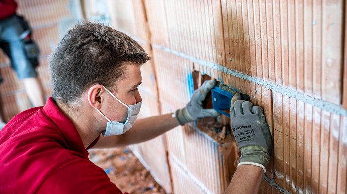 Green Pass: vielleicht schon bald Erleichterungen für Unternehmen Handwerker mit Mundschutz montiert Steckdosenrahmen in Ziegelwand