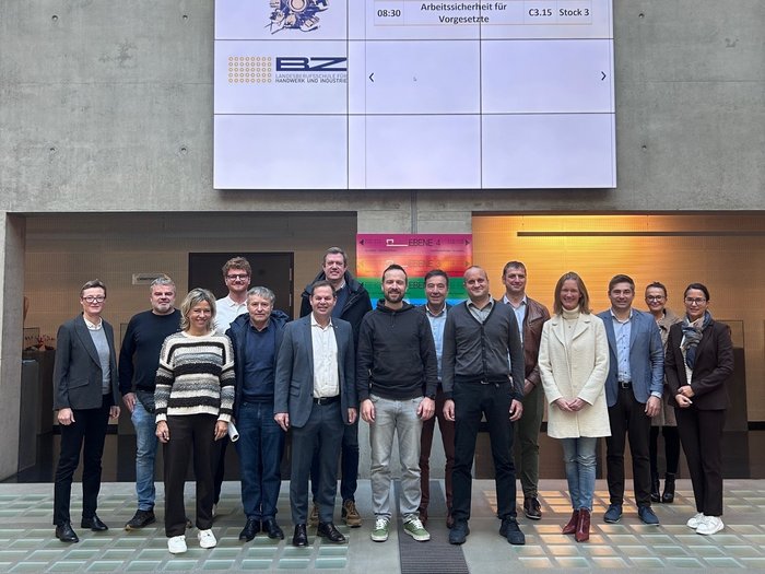 Treffpunkt Schule: Gemeinsam Perspektiven für junge Talente schaffen Gruppenfoto von 15 Personen in einem modernen Gebäude mit digitaler Anzeigetafel