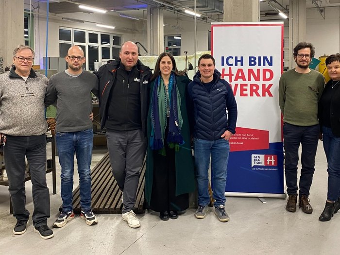 Ortsversammlung der Handwerker/innen in Auer: Zukunft, Innovation und Gemeinschaft im Fokus Sieben Personen stehen in einer Werkstatt vor einem Ich bin Handwerk Banner