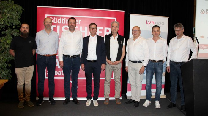 Fachkräftegewinnung im Fokus Gruppenfoto von neun Männern bei einer Tischlerveranstaltung vor Bannern