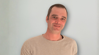 News Mann mit beigem Pullover vor hellem Hintergrund