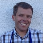 Ricamatori in cuoio Uomo sorridente con camicia a quadri e grembiule blu davanti a muro bianco