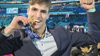 News Junger Mann bei Sportveranstaltung beißt auf Goldmedaille und hebt Arm zum Jubeln