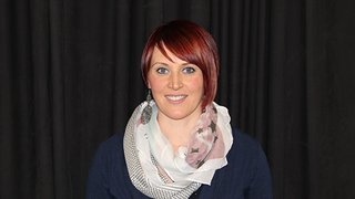 News Porträt einer Frau mit kurzem roten Haar und Schal vor schwarzem Hintergrund