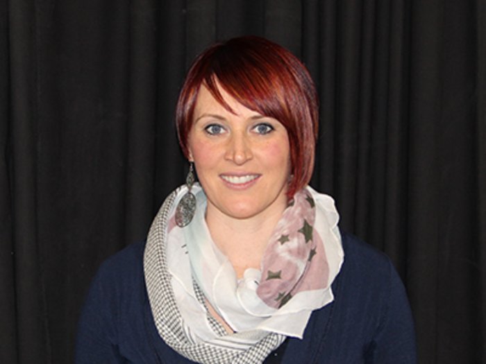 Körperpflegeberufe: Ab Montag endlich wieder an die Arbeit Porträt einer Frau mit kurzem roten Haar und Schal vor schwarzem Hintergrund