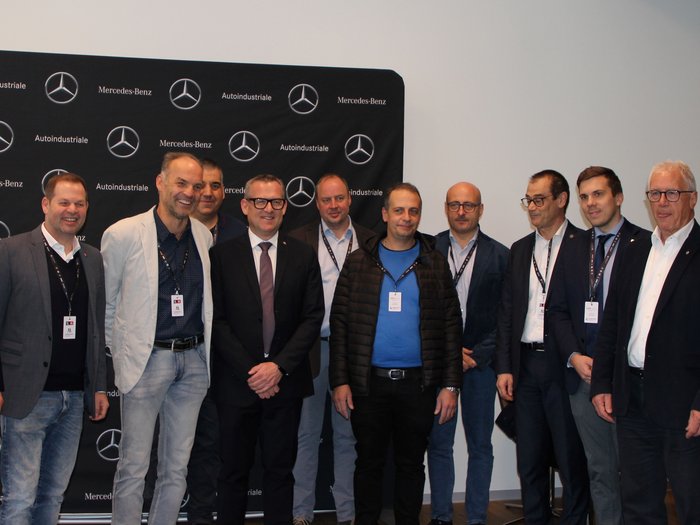 Trasportatori di merci: visione del futuro e sfide attuali Gruppo di dodici uomini davanti a sfondo Mercedes-Benz e Autoindustriale