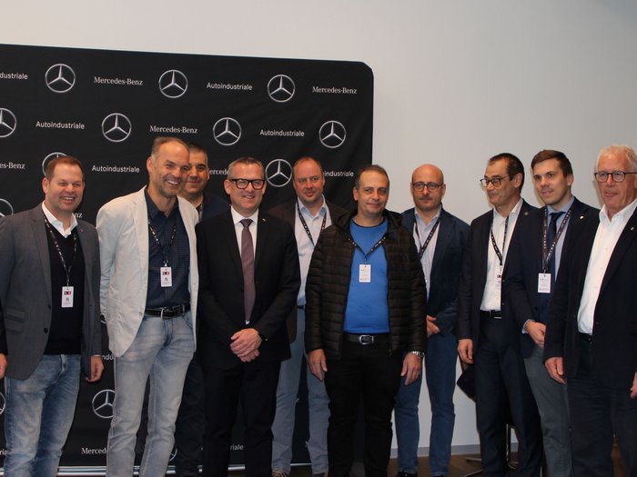 Warentransporteurinnen und -transporteure: Zukunftsvision und aktuelle Herausforderungen Gruppe von zwölf Männern steht vor Mercedes-Benz und Autoindustriale Hintergrund