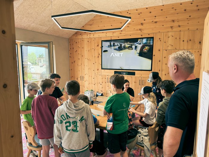 “Anpacken und Gewinnen” (“Affronta e vinci”): il primo parcour dei mestieri artigianali ad Appiano è un'ispirazione! Bambini e adulto in attività di gruppo in una stanza di legno con schermo