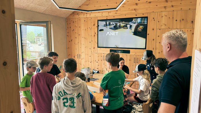 „Anpacken und Gewinnen“ – Eppans erster Handwerksparkour begeistert! Kinder und Erwachsener bei Gruppenaktivität in einem Holzraum mit Bildschirm