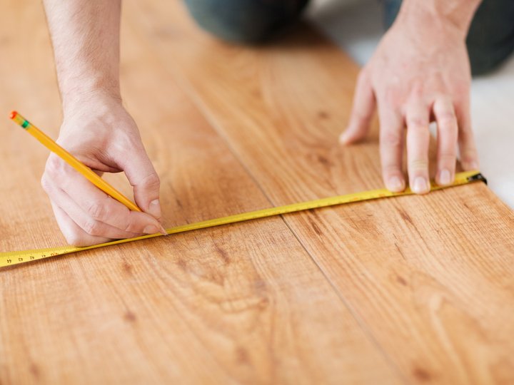 Tischler Person misst und markiert Laminatboden mit Maßband und Bleistift
