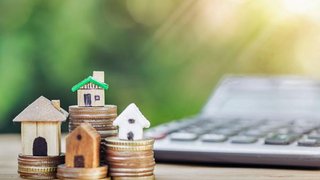 News Miniaturhäuser auf Münzstapeln mit Taschenrechner im Hintergrund