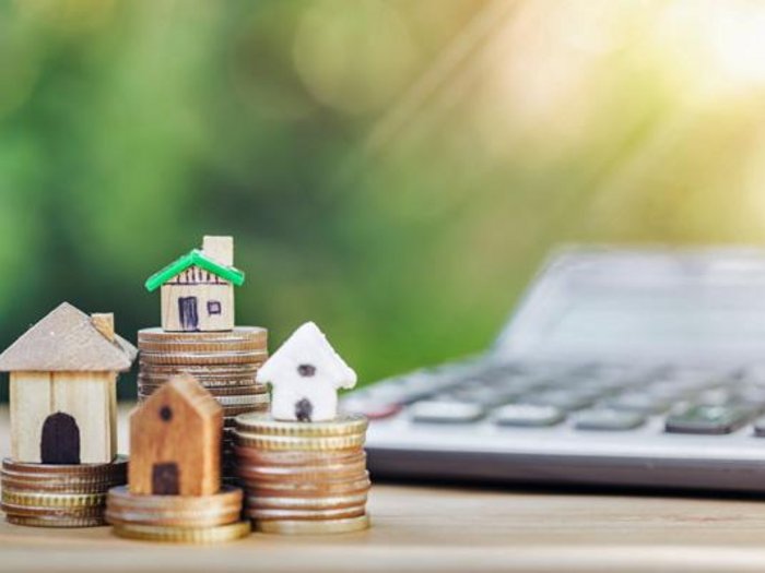 Leistbares Wohnen Miniaturhäuser auf Münzstapeln mit Taschenrechner im Hintergrund