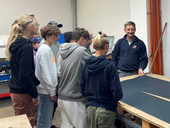 Mittelschule Welsberg: Jugendliche entdecken Berufe im Handwerk und Gastgewerbe Gruppe Jugendlicher hört einem Mann bei einer Vorführung in einer Werkstatt zu