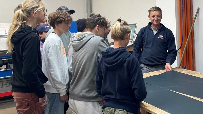Mittelschule Welsberg: Jugendliche entdecken Berufe im Handwerk und Gastgewerbe Gruppe Jugendlicher hört einem Mann bei einer Vorführung in einer Werkstatt zu