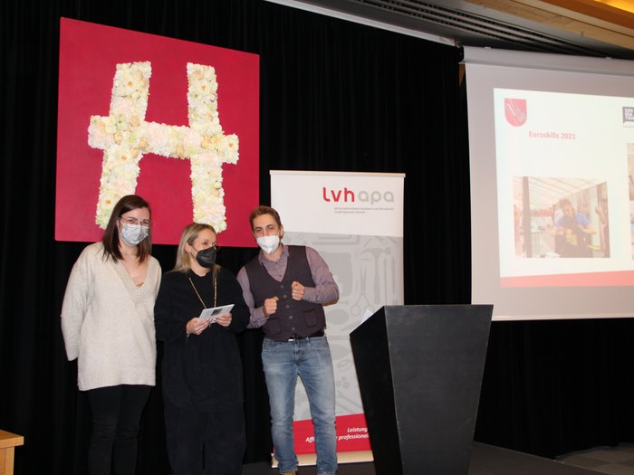 Mit Zuversicht ins Frühjahr Drei Personen mit Masken stehen vor einem lvh apa Banner und einer Leinwand