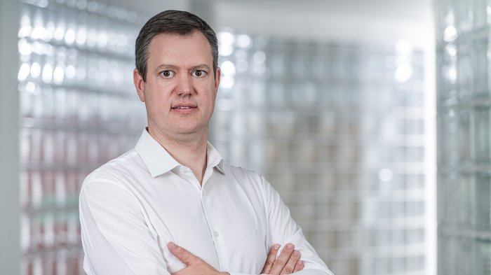 Arbeitssicherheit: Neue Maßnahmen müssen praxisnah und differenziert sein Mann mit weißem Hemd steht mit verschränkten Armen vor verglaster Wand